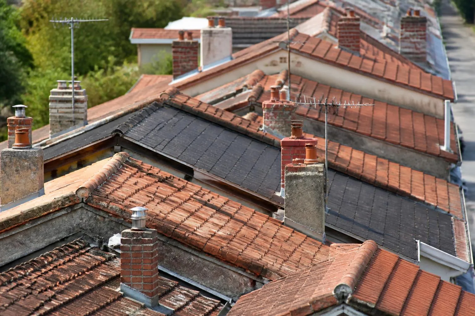 Toitures de pavillons alignées vues depuis un point haut, tuiles et ardoises mêlées.