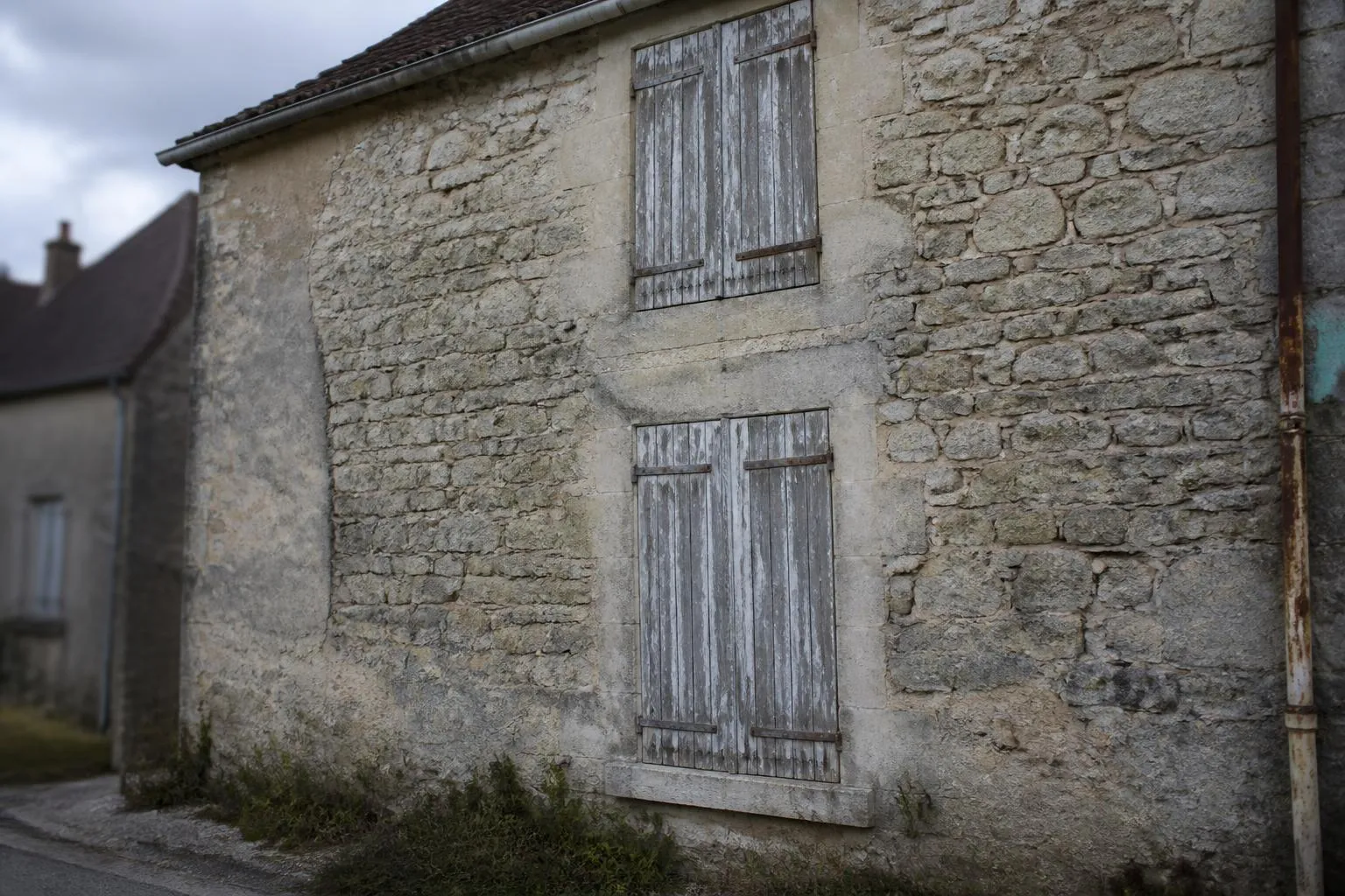 Volets de bois fermés et écaillés sur la façade en pierre d'une maison de bourg